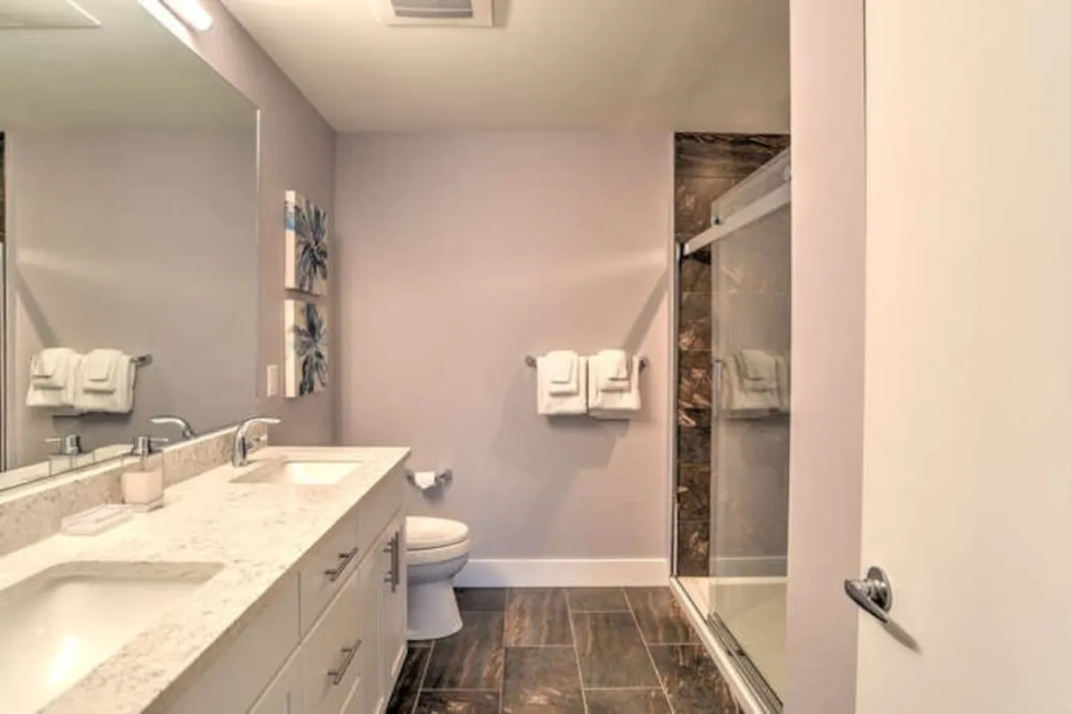 A modern bathroom with a spacious double vanity, a sleek glass-enclosed shower, and decorative wall art. Ample natural light creates a calming ambiance, making it ideal for morning routines or relaxing evening baths.