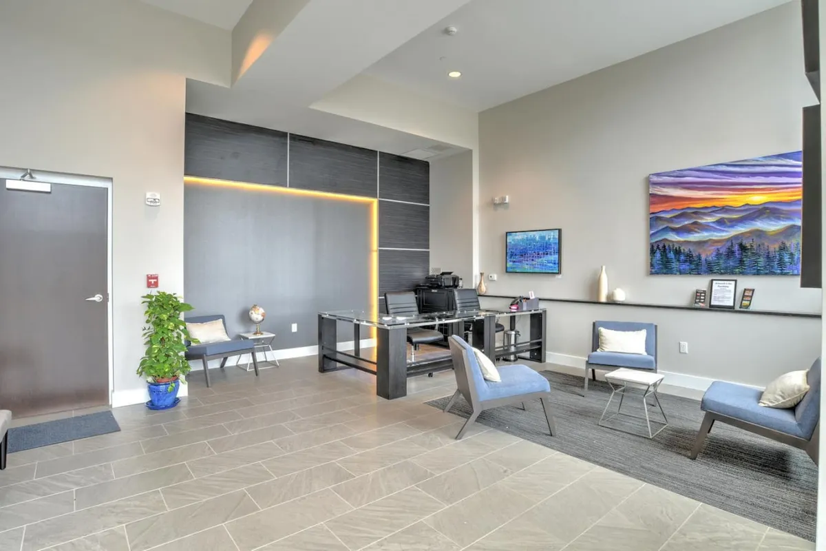 The image shows a modern reception area within the building, featuring a sleek reception desk, contemporary artwork on the wall, and a comfortable seating area. The space is designed to welcome guests while highlighting professional management and secure entry.