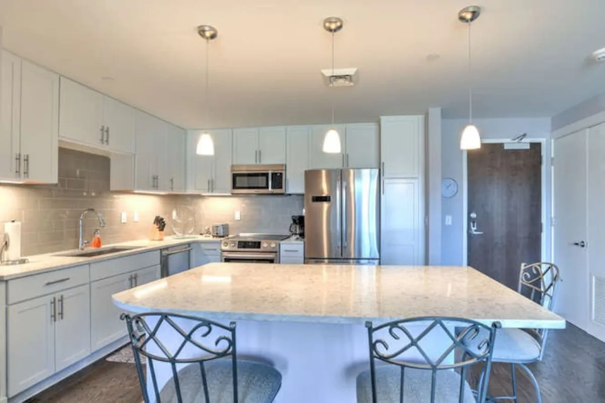 An open kitchen featuring an island countertop, stainless steel appliances, and stylish hanging light fixtures. The design invites communal cooking and entertaining, supporting gatherings and culinary creativity.