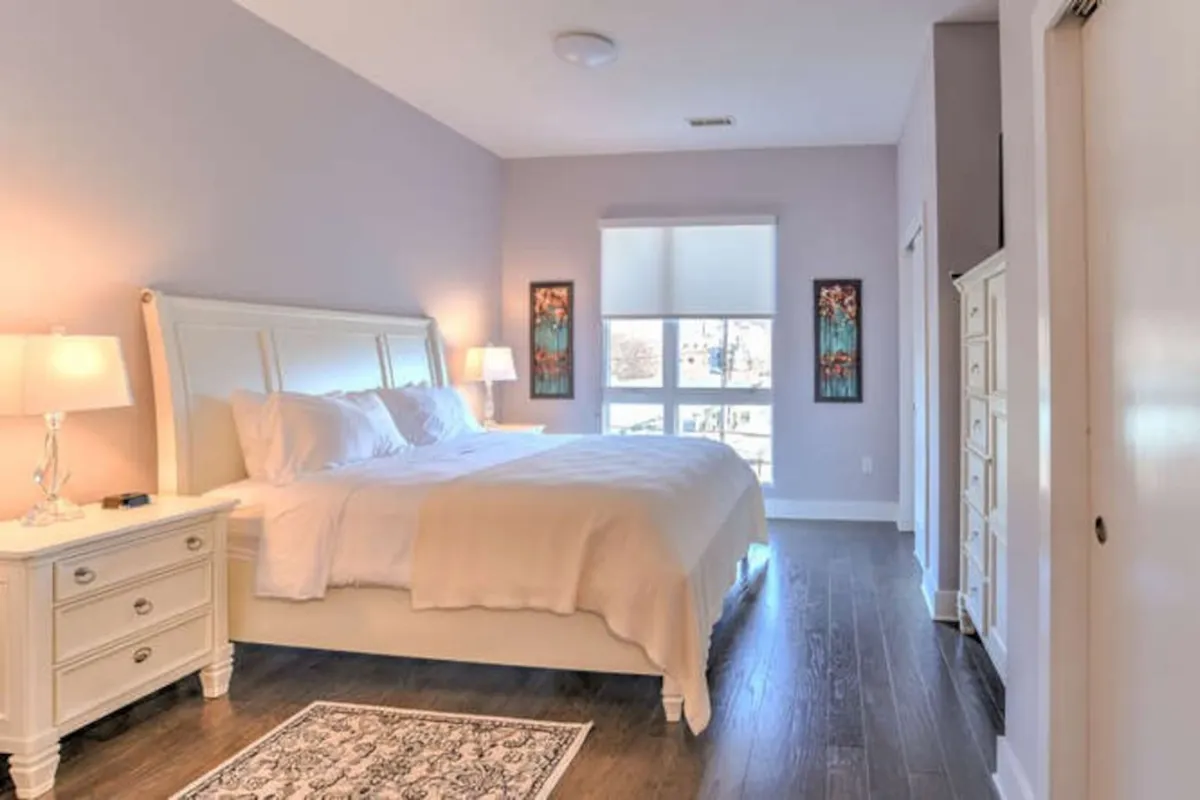 A stylish king bedroom with a comfortable bed, well-appointed nightstands, a large window bathing the space in daylight, and decorative wall art. The atmosphere is peaceful, ideal for unwinding with a book or enjoying a restful sleep.