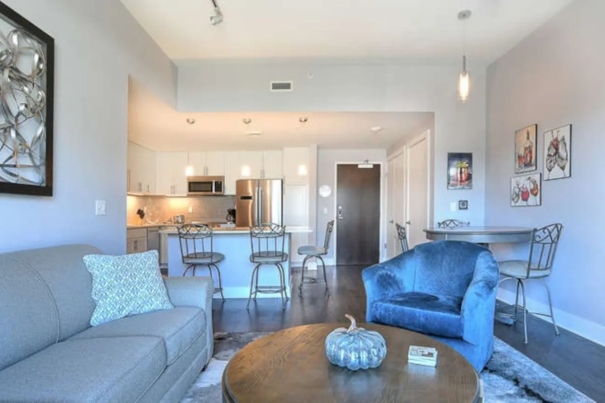 An open-concept space that blends the living room, blue accent chair, dining area, and kitchen island into one cohesive environment. The sofa and armchair are ready for relaxation, while the adjacent kitchen and dining area suggest easy transitions for entertaining or gathering with friends.