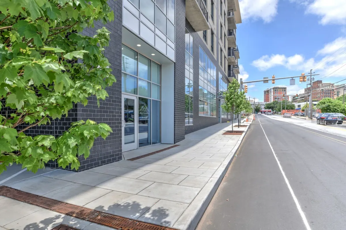 The image features a modern building facade surrounded by trees and a wide sidewalk, capturing the lively, accessible atmosphere of the property’s exterior. It hints at the availability of parking and effortless urban access.