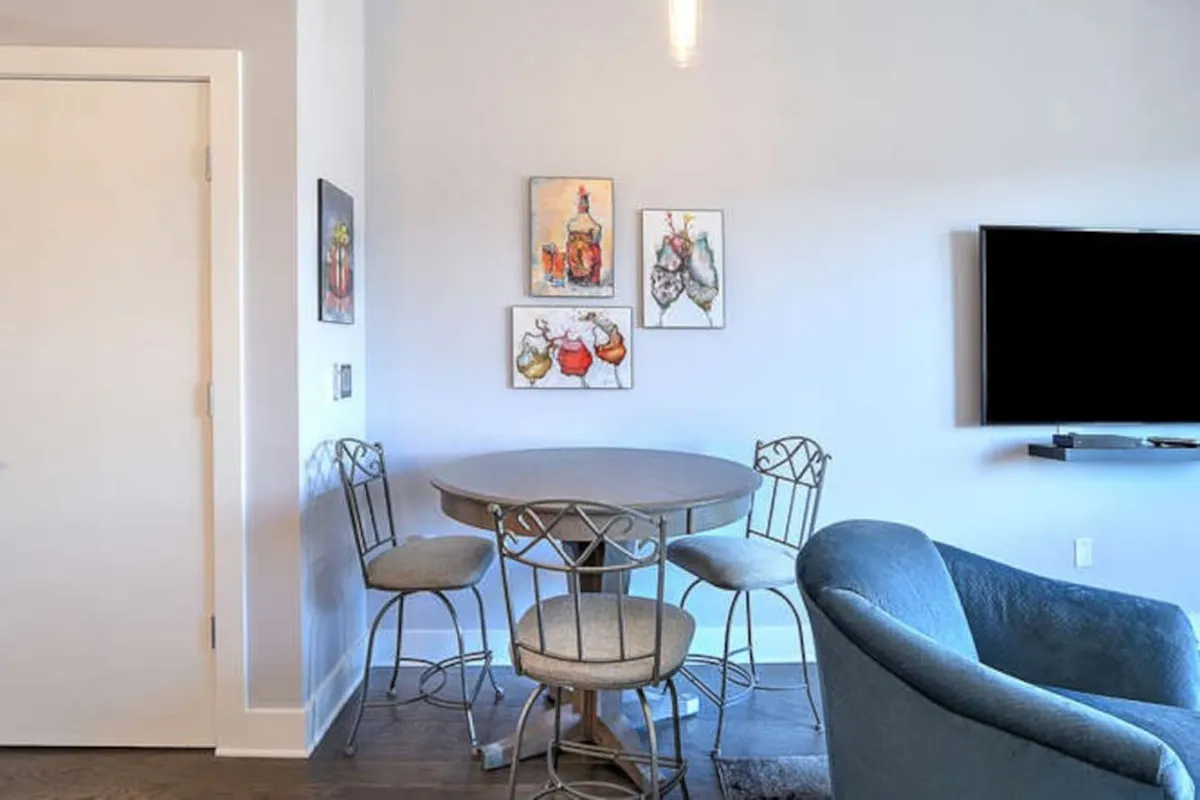 A cozy dining area with a round table set beneath decorative wall art, adjacent to a television. The setting encourages intimate dining, conversation, and shared moments in a relaxed, artful environment.