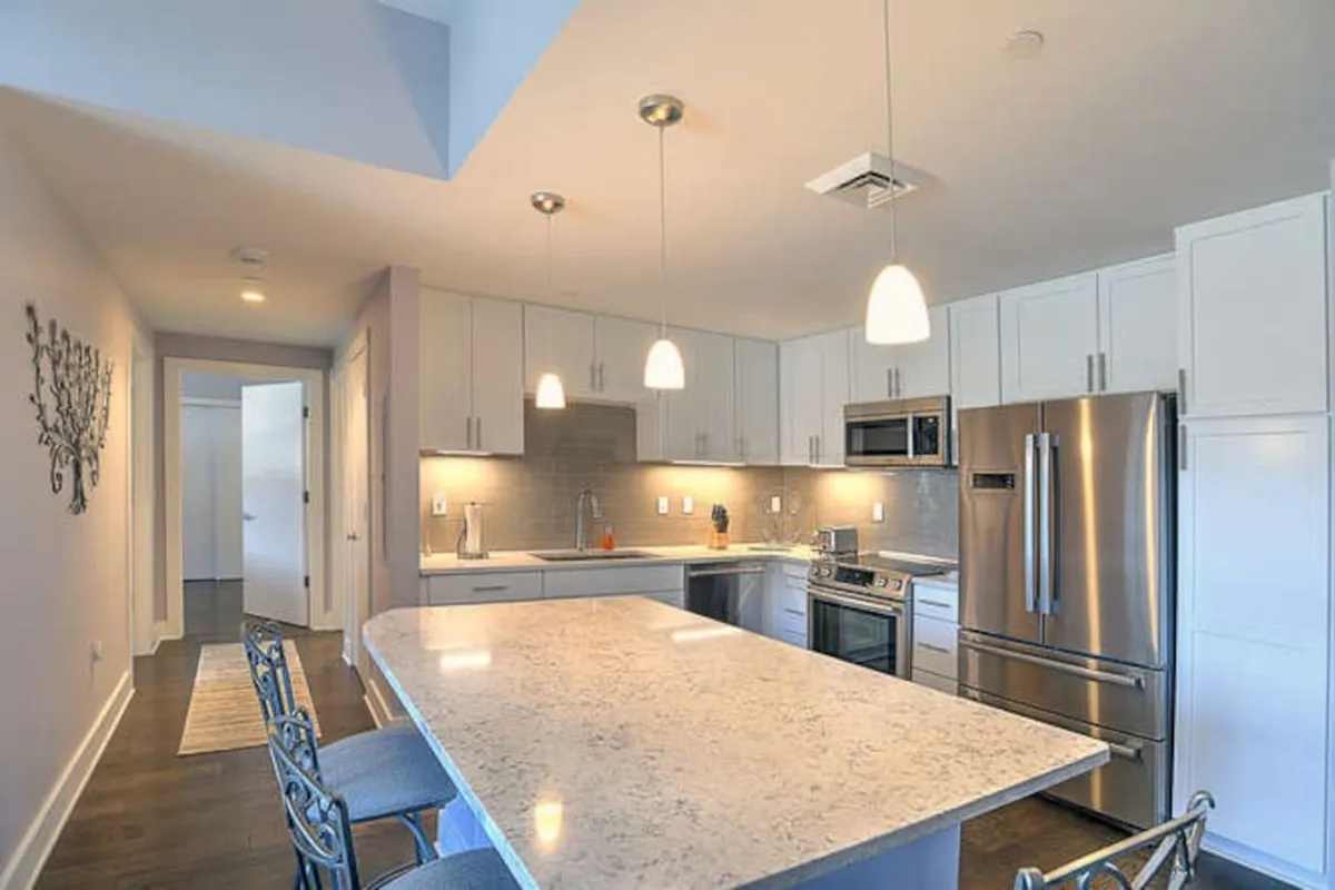 This image features a spacious kitchen with a central island countertop, sleek stainless steel appliances, and stylish pendant lighting. The open layout is ideal for both preparing meals and entertaining, with contemporary finishes that create a warm, inviting atmosphere.