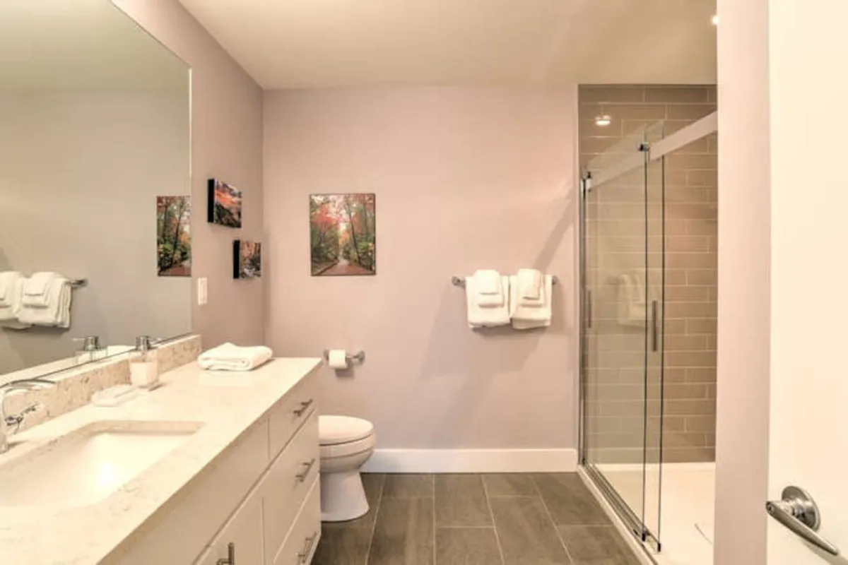 A calm, refreshing bathroom scene with a mirror, vanity, shower, and tasteful artwork. The space is bright and thoughtfully designed, suggesting a restorative place for personal preparation before or after meetings.